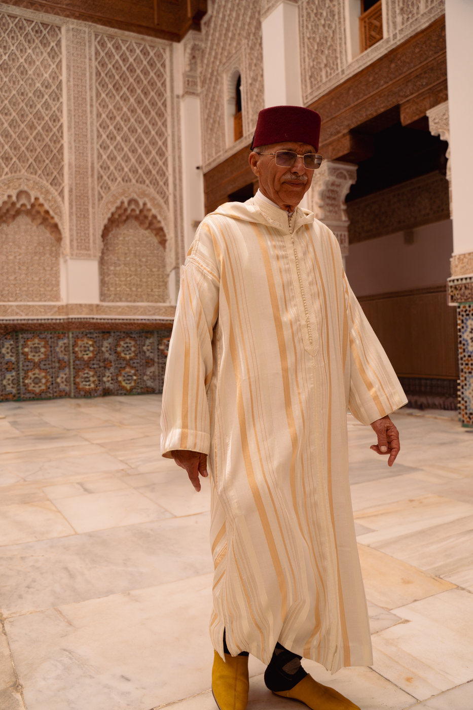 A man in a white robe in a tiled courtyard, in a 4:5 frame
